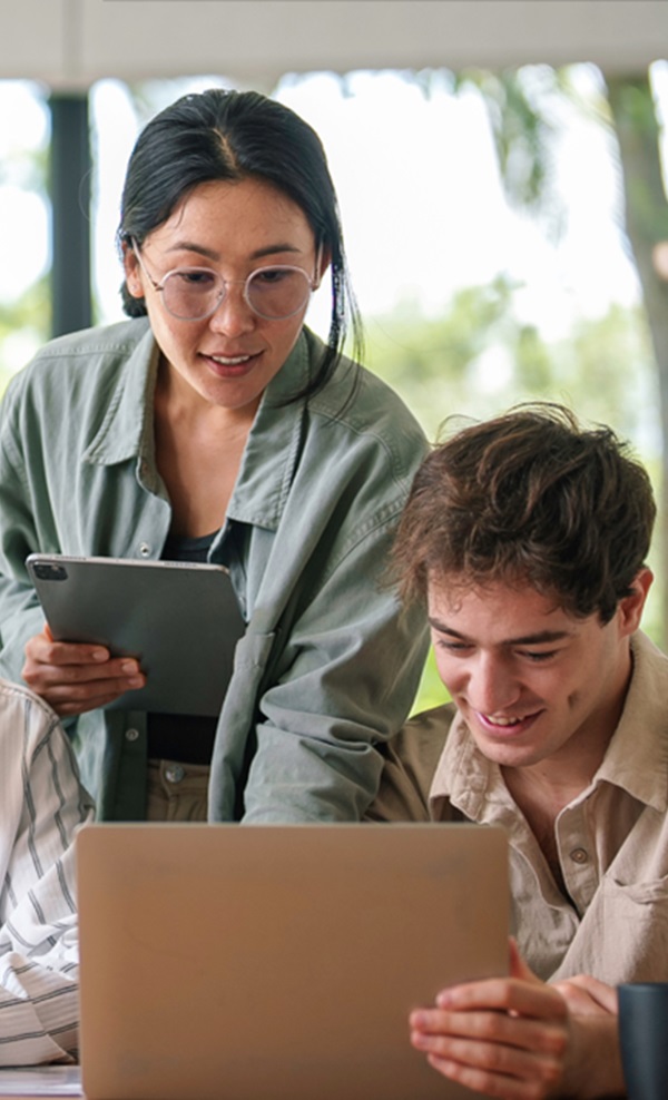 Three coworkers collaborate using various devices such as a laptop and tablets.