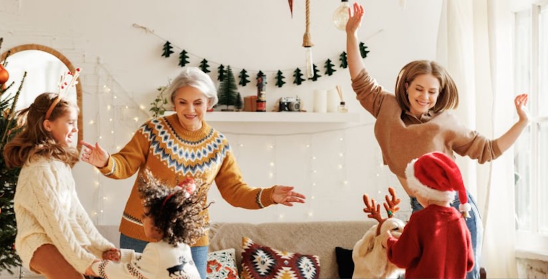 Happy positive family with three kids and golden retriever have fun on Christmas day at home. Mother, grandmother and multiethnic children dance together during winter holidays
