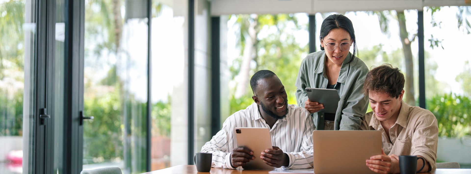 Three coworkers collaborate using various devices such as a laptop and tablets.