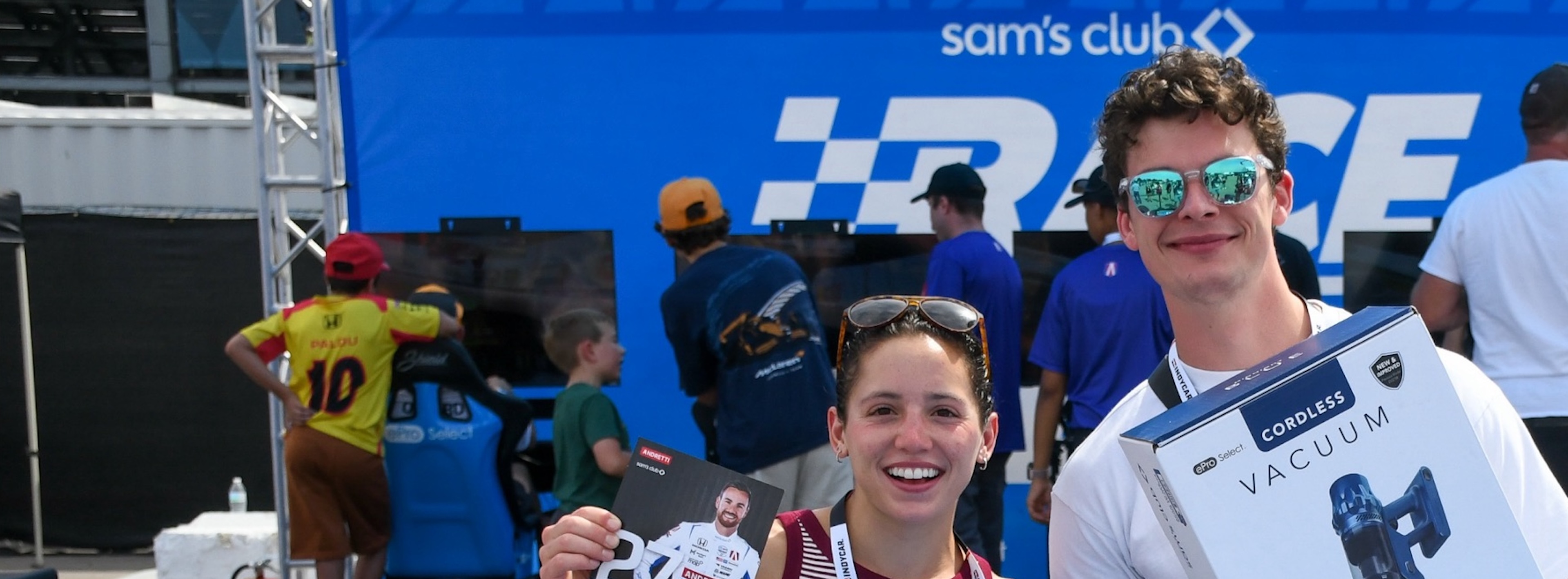 Two happy young people smile while holding products in front of a Sam's Club special event.