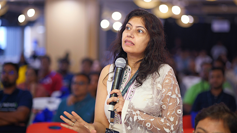 A female audience member talking into the microphone in her hand. There are several other audience members in the background. 