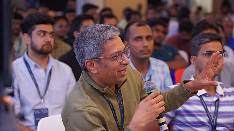 A male audience member talking into the microphone in his hand. There are several other audience members in the background. 